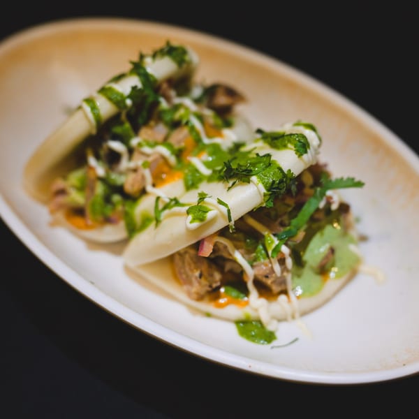Three Indian-style bao buns filled with meat, green sauce, and white drizzle on a white plate.