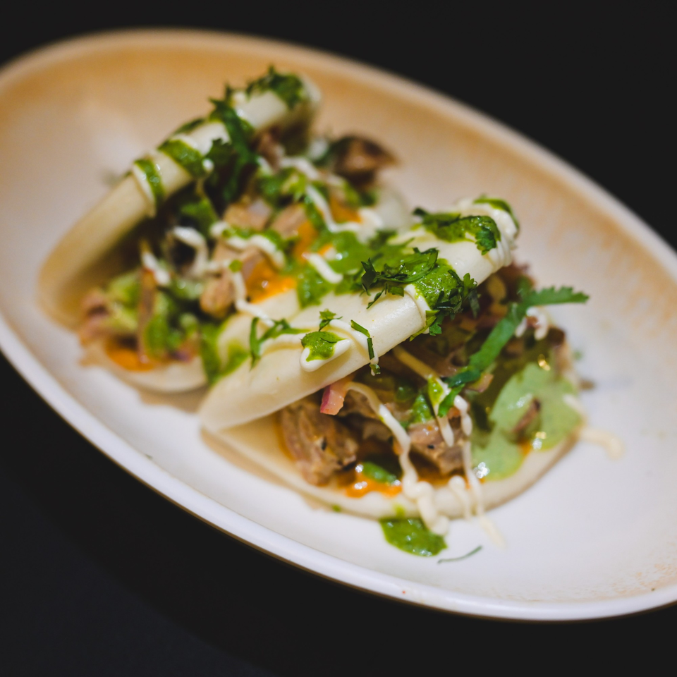 Three Indian-style bao buns filled with meat, green sauce, and white drizzle on a white plate.