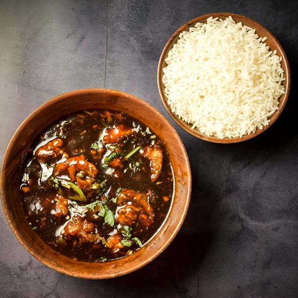 Indian chili chicken with cilantro and white rice in wooden bowls on a dark surface.