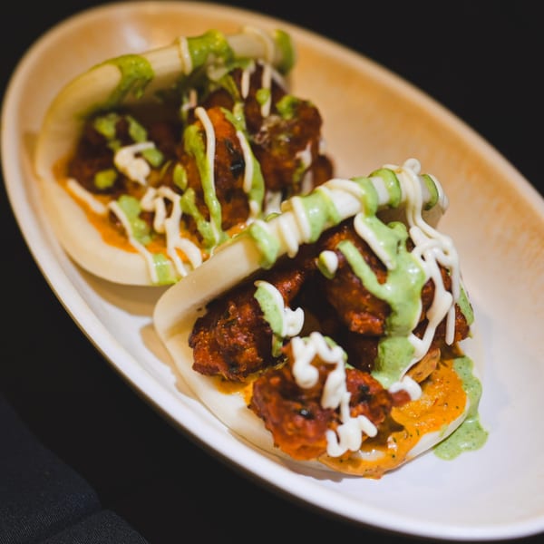 Two Indian chicken bao buns with green and white sauces on a white plate.