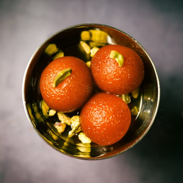 Three gulab jamun, garnished with pistachios, in a metal bowl from The Monk's Indian Bistro.