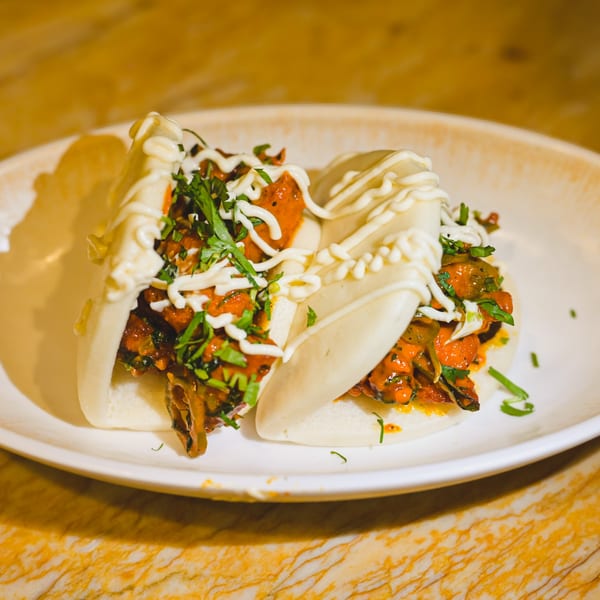 Two Indian-style bao buns filled with chicken tikka, drizzled with white sauce and fresh cilantro.