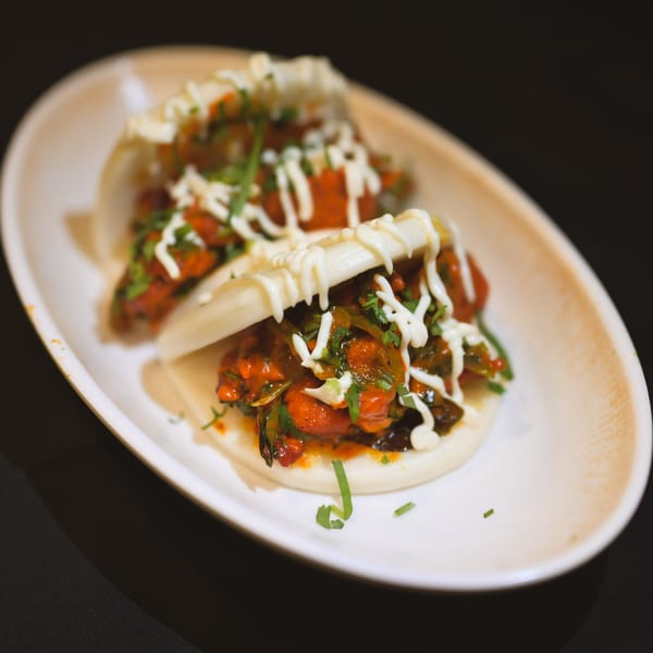 Two Indian chicken bao buns with sauce and cilantro on a white plate.