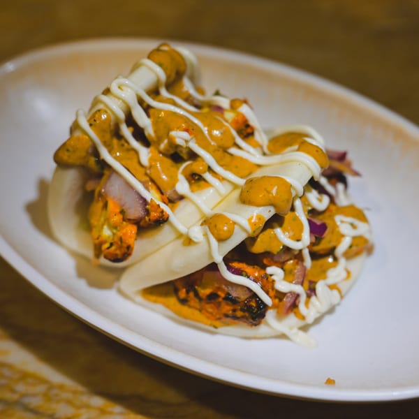 Indian bao buns with chicken, red onions, and two sauces on a white plate.