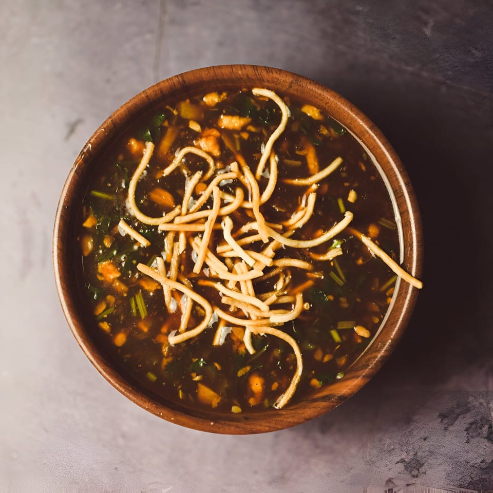 Overhead view of a wooden bowl filled with Indian hot and sour soup, topped with crispy noodles.