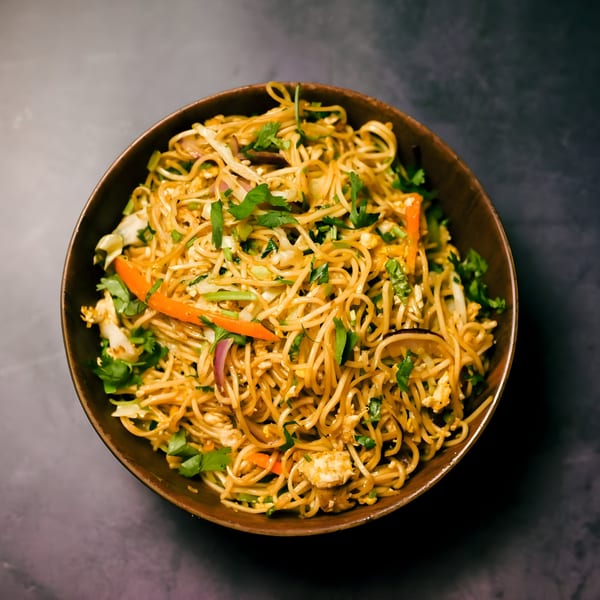A close-up, overhead view of a bowl of Indian noodles with vegetables and cilantro.