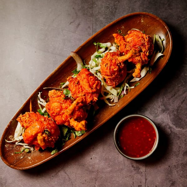 Indian chicken lollipops, garnished with herbs and cabbage, served with a red dipping sauce.
